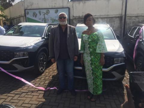 First lady and the donor pose for a photo with vehicles in the background